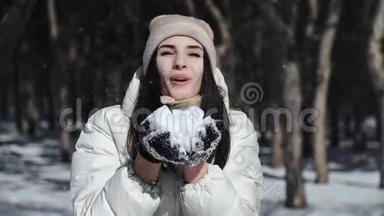 一个黑发女孩穿着白色羽绒服，戴着冬手套，手里拿着雪，吹着雪